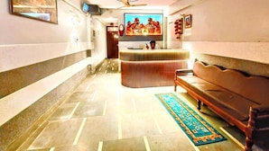 A hotel lobby with a reception desk, a sofa, a television, and a patterned rug. - Trinetra Nirvana (varanasi)