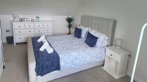A bedroom with a bed, bedside tables, a dresser, a ceiling fan, and a nightstand. - Large Guest Room with Kingsize Bed & Private Bathroom (Roundswell)