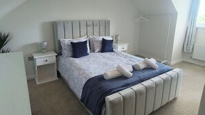 A bedroom with a large bed, a bedside table, a hanging light, and a window with curtains. - Large Guest Room with Kingsize Bed & Private Bathroom (Roundswell)
