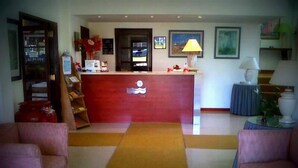 Un espace d’accueil avec un comptoir rouge, un bureau de réception, une petite table bleue avec une lampe et deux fauteuils roses.