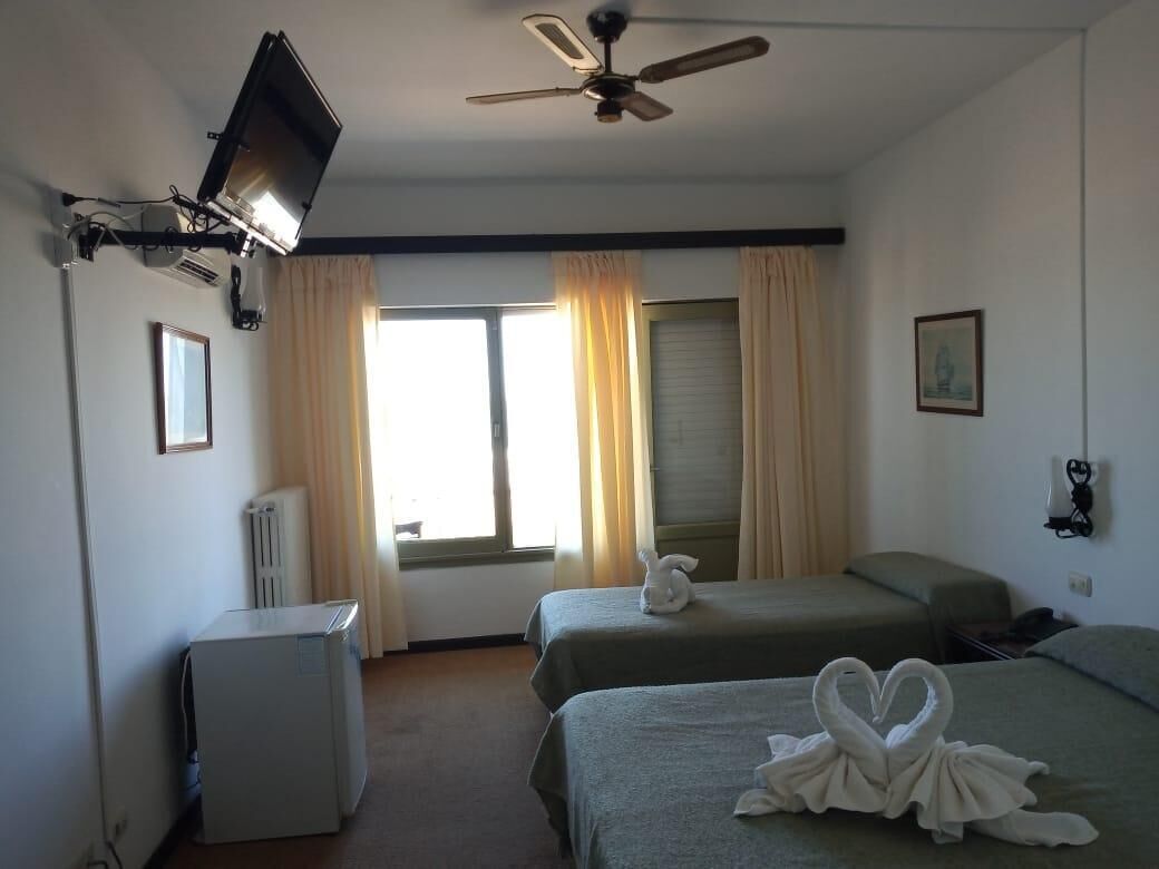 Habitación de hotel con dos camas, ventilador de techo, televisión montada en la pared y radiador.