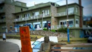 Une statue représentant une personne assise sur un banc, avec une pancarte placée en avant-plan.