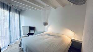 A bedroom with a bed, a chair, a bedside table, a lamp, and a window with curtains.