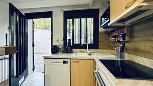 A compact kitchen with a dishwasher, a stove, and a sink. There are windows with vertical blinds, and a small countertop with kitchen appliances.
