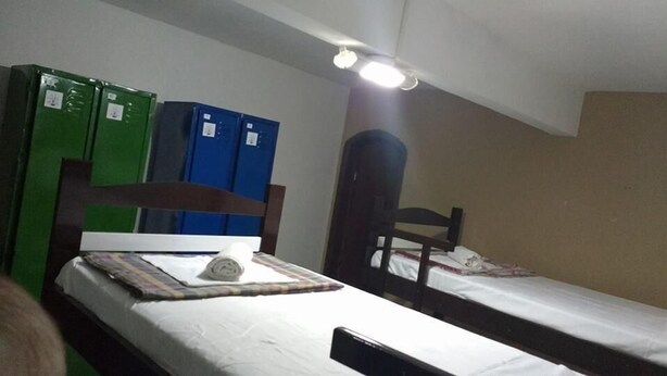 A small, dimly lit room with two beds, a wooden headboard, and a ceiling light. - Green Special B&B (Rio de Janeiro)