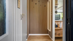 Un pasillo con un panel de madera con listones, una puerta con manija de latón y un pequeño estante con un hervidor y un rollo de toallas de papel.
