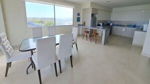 Eine moderne Küche mit weißen Schränken, ein Essbereich mit einem Glastisch und Blick durch große Fenster.