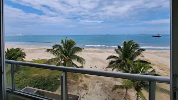 Blick auf einen Strand vom Balkon aus, mit Palmen und einem Boot in der Ferne.