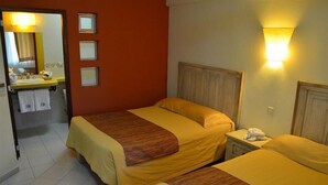 Ein Hotelzimmer mit zwei Betten, einem Badezimmer mit Spiegel und einem Nachttisch mit Lampe.