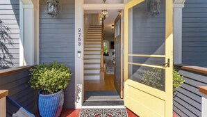 Une entrée de maison avec le numéro « 2753 » affiché sur le mur, un escalier en bois et une porte jaune munie d’une moustiquaire.