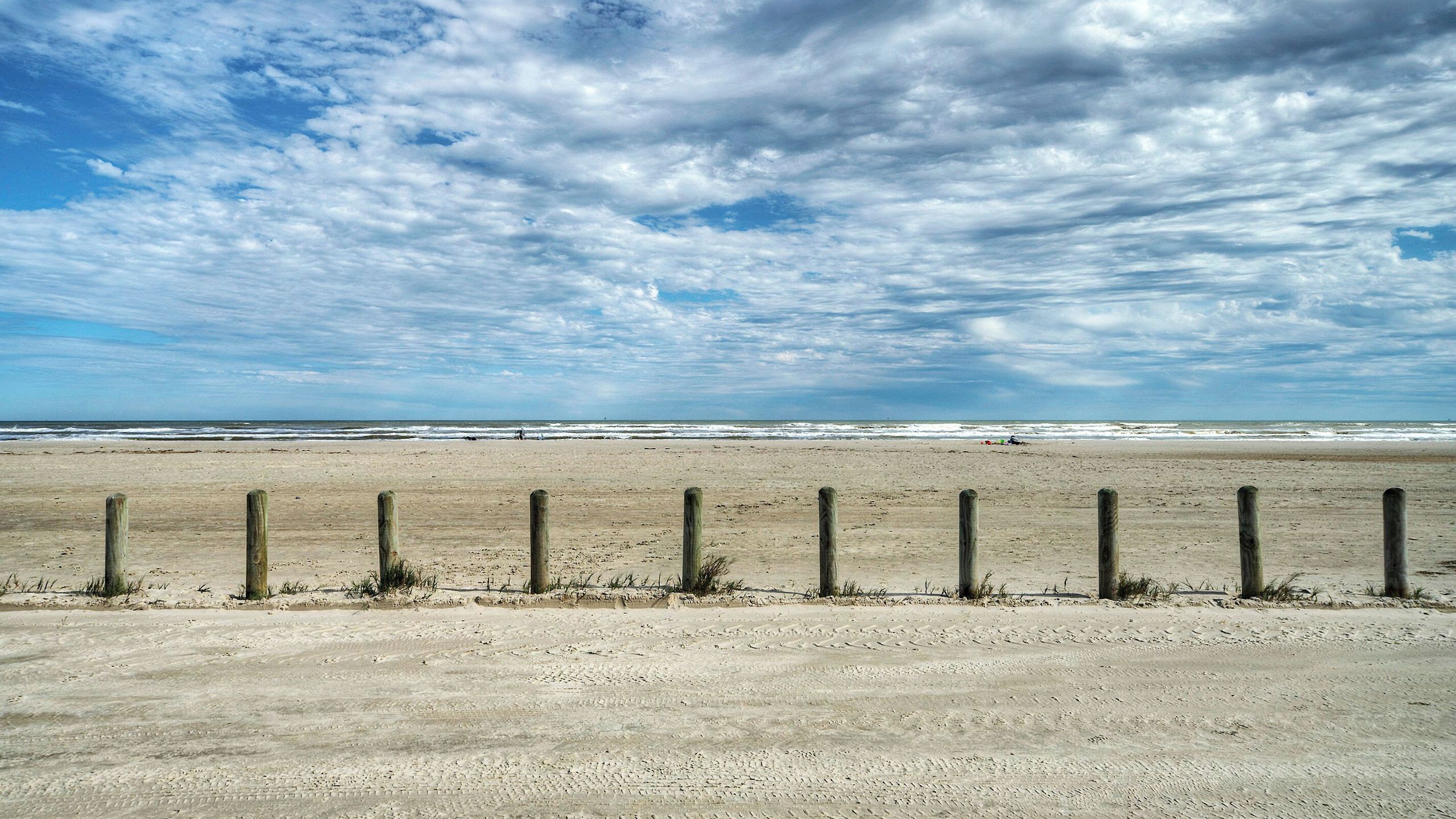 A beach with a sandy shore, wooden posts, and the ocean in the background.
