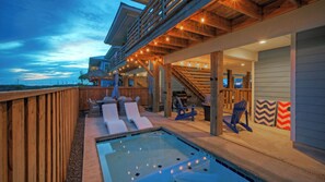 Un espace piscine avec des chaises longues, un jacuzzi et une terrasse couverte agrémentée de guirlandes lumineuses.