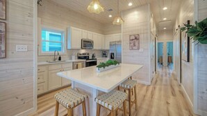 A modern kitchen with wooden paneling, stainless steel appliances, and a central island with bar stools. - Private Pool, Fire Pit, Beach Boardwalk Access, Views The Madison by Avantstay (Port Aransas)