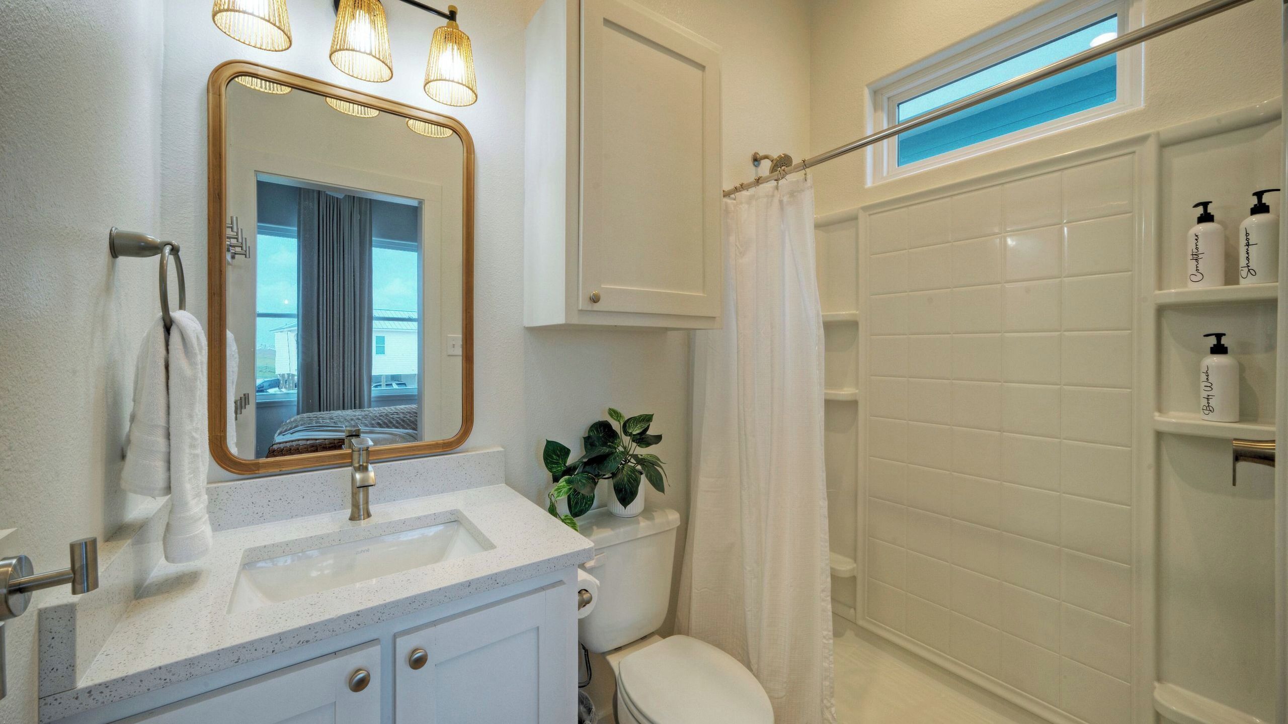 A bathroom with a sink, mirror, toilet, shower, and a potted plant.