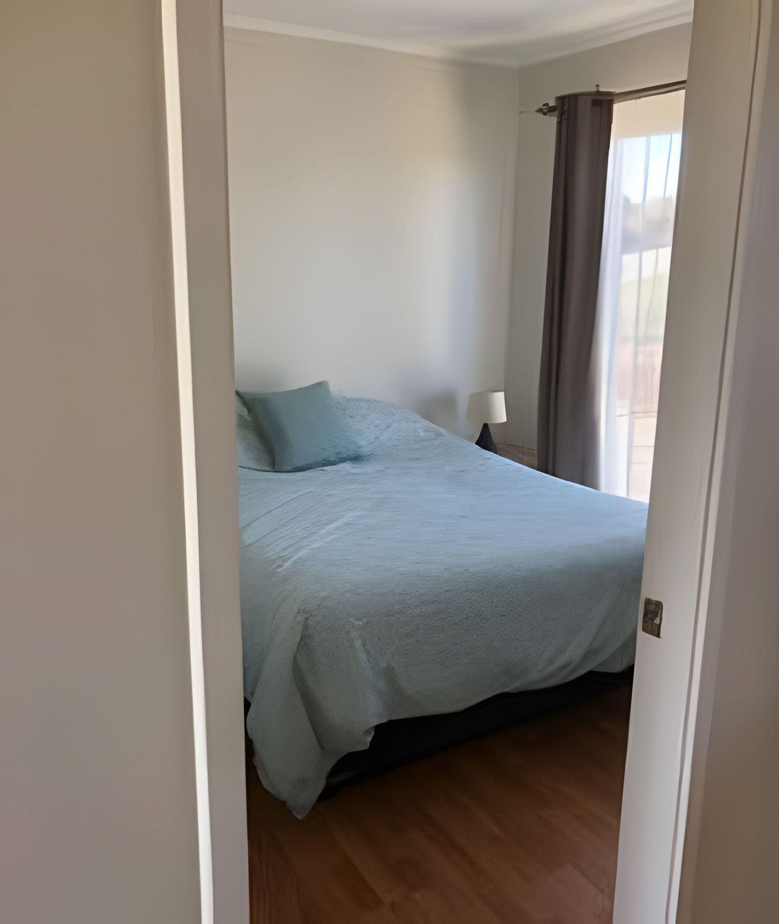 A bedroom with a bed, a nightstand, and a window with curtains.