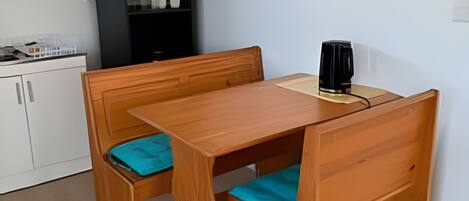 A wooden dining table with benches, a black speaker, and a white cabinet in a room with light-colored flooring.