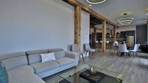 A modern living room with a grey sofa, glass coffee table, and wooden beams. - Sublime 3BR/3BA condo with Parking in the Heart of Old Montreal (Montréal)