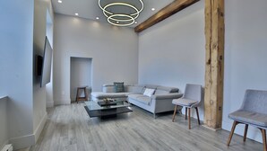 A modern living room with a grey sofa, two armchairs, a coffee table, and a wooden beam. - Sublime 3BR/3BA condo with Parking in the Heart of Old Montreal (Montréal)