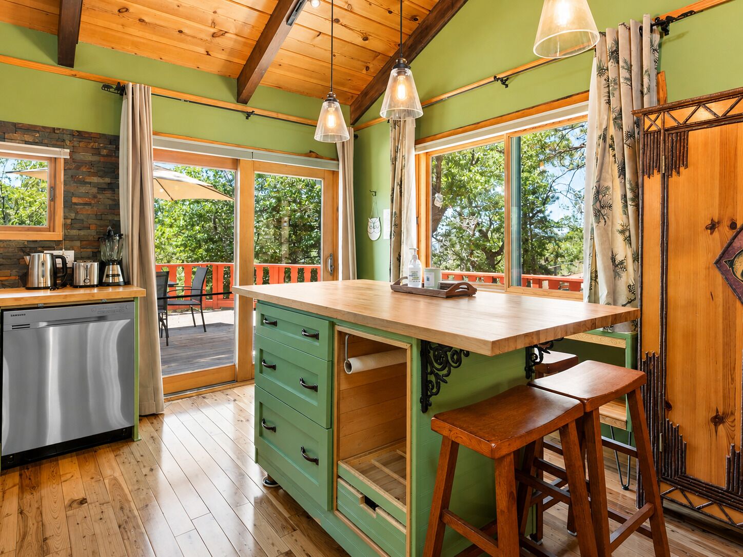 A kitchen with a wooden island, bar stools, a refrigerator, and a window overlooking greenery.