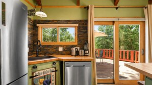 A kitchen with a built-in dishwasher, a refrigerator, a window with a view of trees, and a sliding glass door leading to an outdoor area. - Pinecone Ridge (Big Bear Lake)