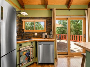 A kitchen with a built-in dishwasher, a refrigerator, a window with a view of trees, and a sliding glass door leading to an outdoor area. - Pinecone Ridge (Big Bear Lake)