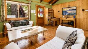 A cozy room with a wooden ceiling, a sofa, a table, and a TV on the wall. - Pinecone Ridge (Big Bear Lake)