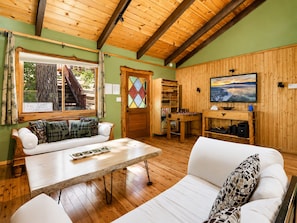 A cozy room with a wooden ceiling, a sofa, a table, and a TV on the wall. - Pinecone Ridge (Big Bear Lake)