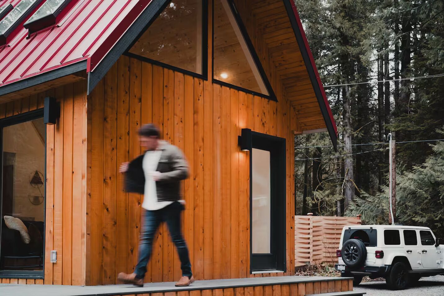 A wooden cabin with a red roof, a black door, and a white SUV parked outside.