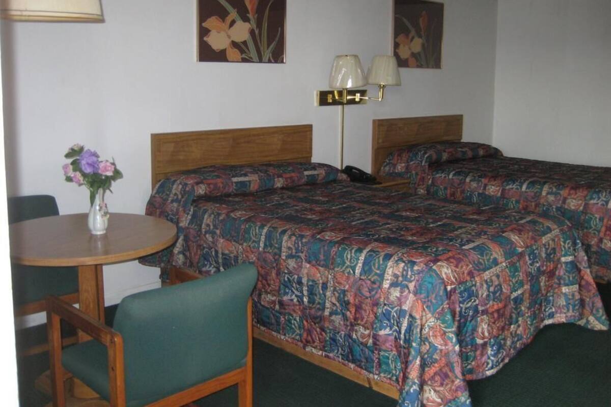 A hotel room with two beds, a round table with a chair, a lamp, and floral artwork on the walls.