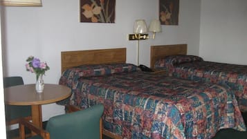 A hotel room with two beds, a round table with a chair, a lamp, and floral artwork on the walls.
