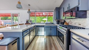 Een moderne keuken met een groot eiland, roestvrijstalen apparatuur en uitzicht op groen.