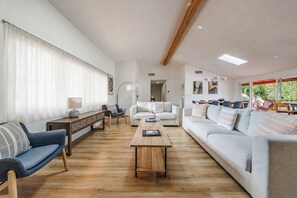 A spacious living room with a sofa, armchair, coffee table, and a dining area with chairs and a table.