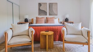 Een slaapkamer met een bed, twee nachtkastjes, twee stoelen, een ronde tafel en twee decoratieve wandobjecten.