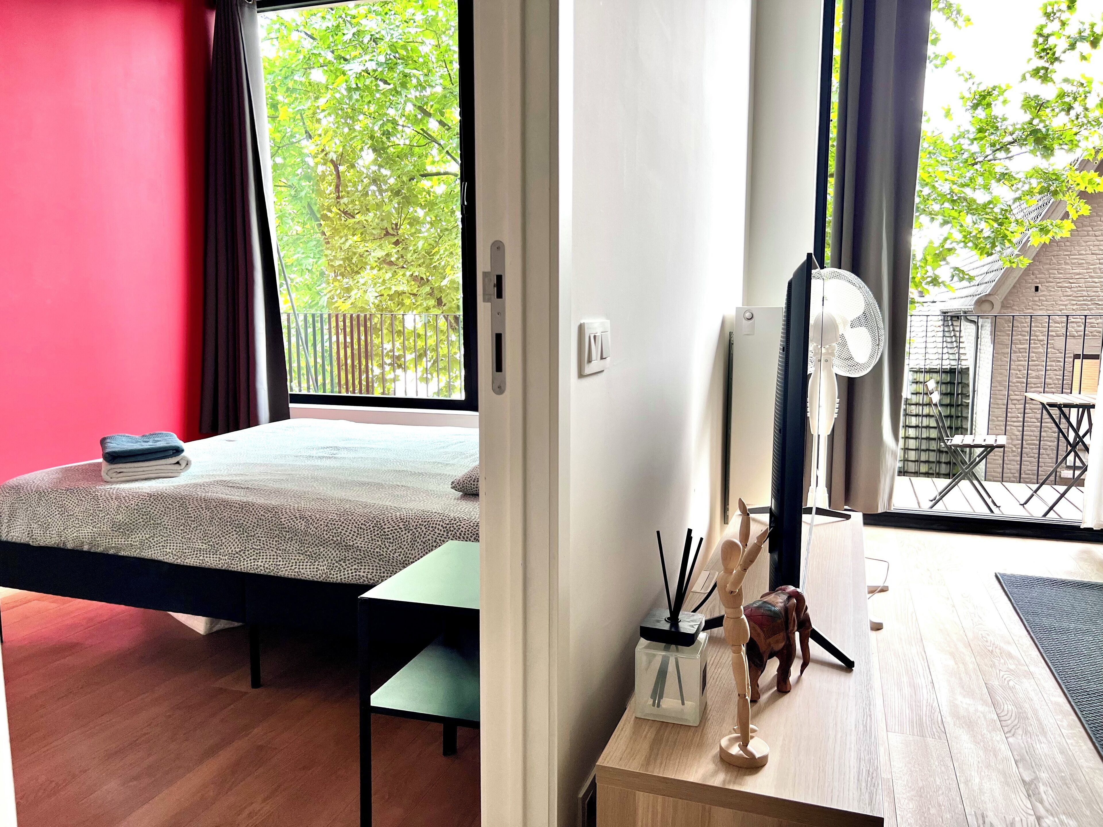 Une chambre à coucher comprenant un lit, un bureau, une chaise, un ventilateur et donnant sur l’extérieur.