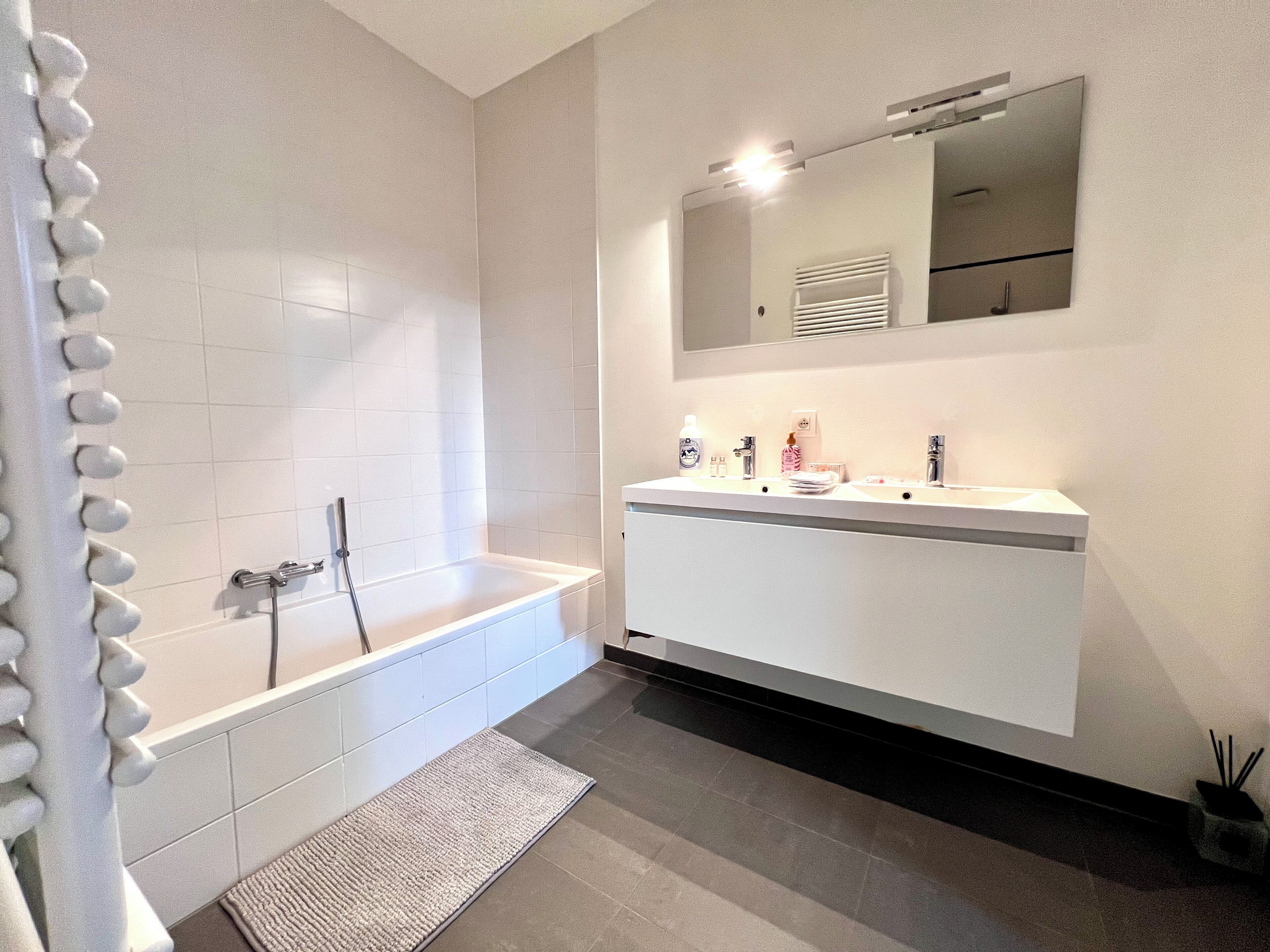 Une salle de bain moderne avec une baignoire, un grand miroir et un meuble-lavabo blanc.