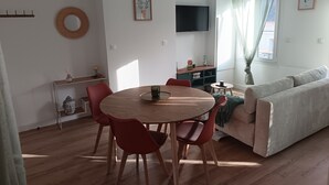 A modern living room with a round wooden dining table, red chairs, a beige sofa, and a TV mounted on the wall. - Renovated duplex - Harbour view (Saint-Valery-en-Caux)