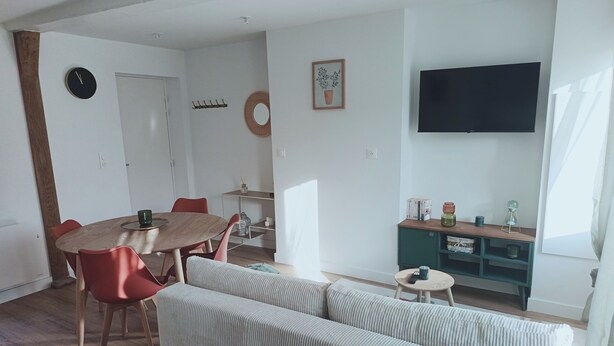 A modern living room with a round wooden dining table, red chairs, a grey sofa, and a TV mounted on the wall. - Renovated duplex - Harbour view (Saint-Valery-en-Caux)