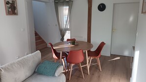 A dining area with a round table, red chairs, a wooden floor, a grey sofa with a green throw, and a staircase leading to another room. - Renovated duplex - Harbour view (Saint-Valery-en-Caux)