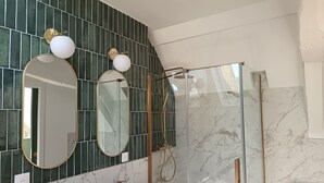 A bathroom with a large mirror, two wall-mounted lights, a glass shower enclosure, and a marble-tiled wall. - Renovated duplex - Harbour view (Saint-Valery-en-Caux)