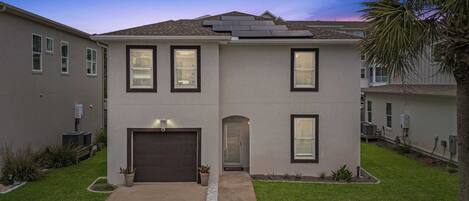 A two-story residential building with a garage, solar panels, and a well-maintained lawn.