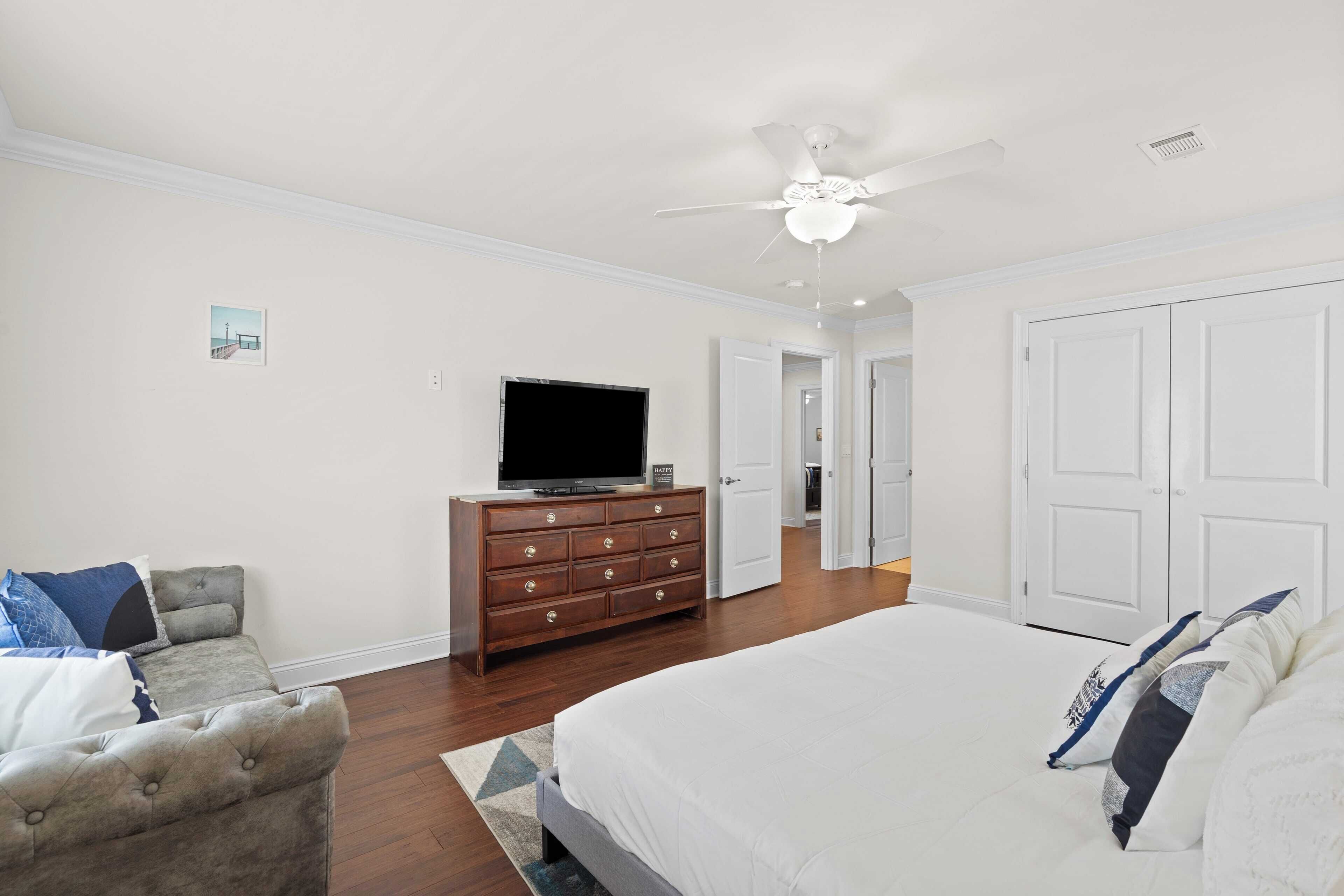 Quarto com cama, penteadeira, televisão e ventoinha no teto.