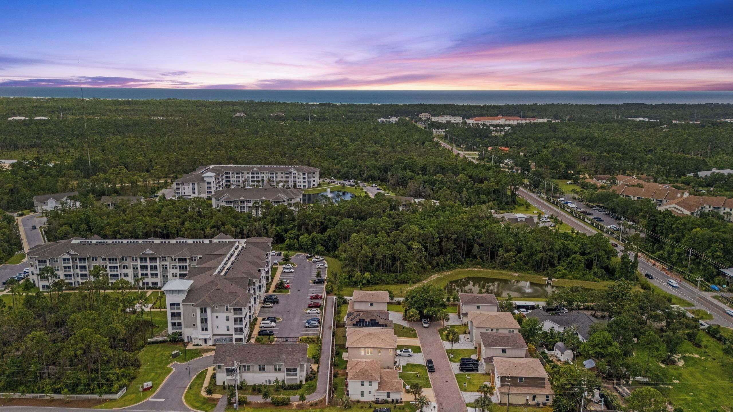 An aerial view of a residential area with a large building complex, roads, and surrounding greenery.
