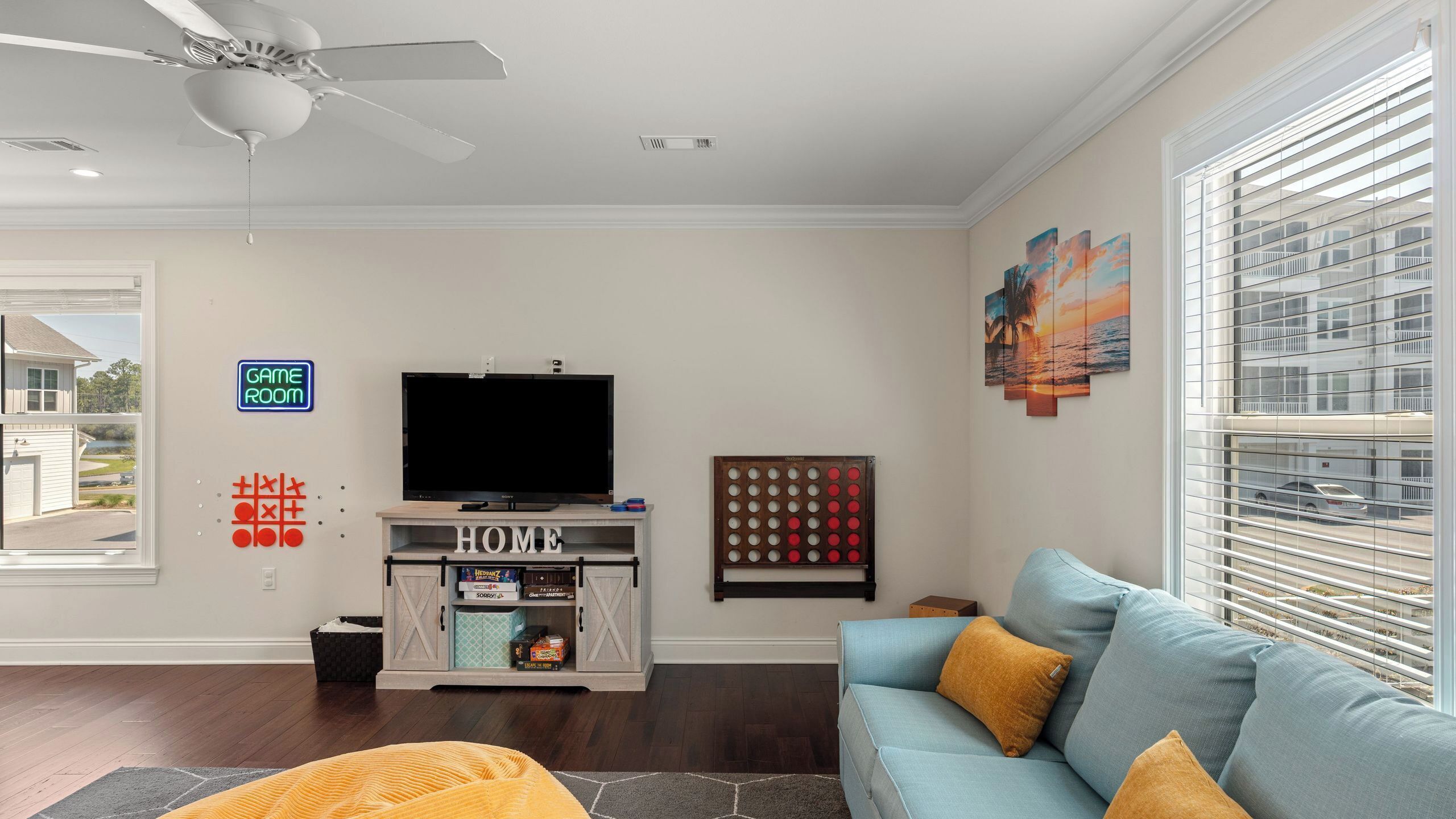 A living room with a TV, a game room sign, a sofa, and a window with blinds.
