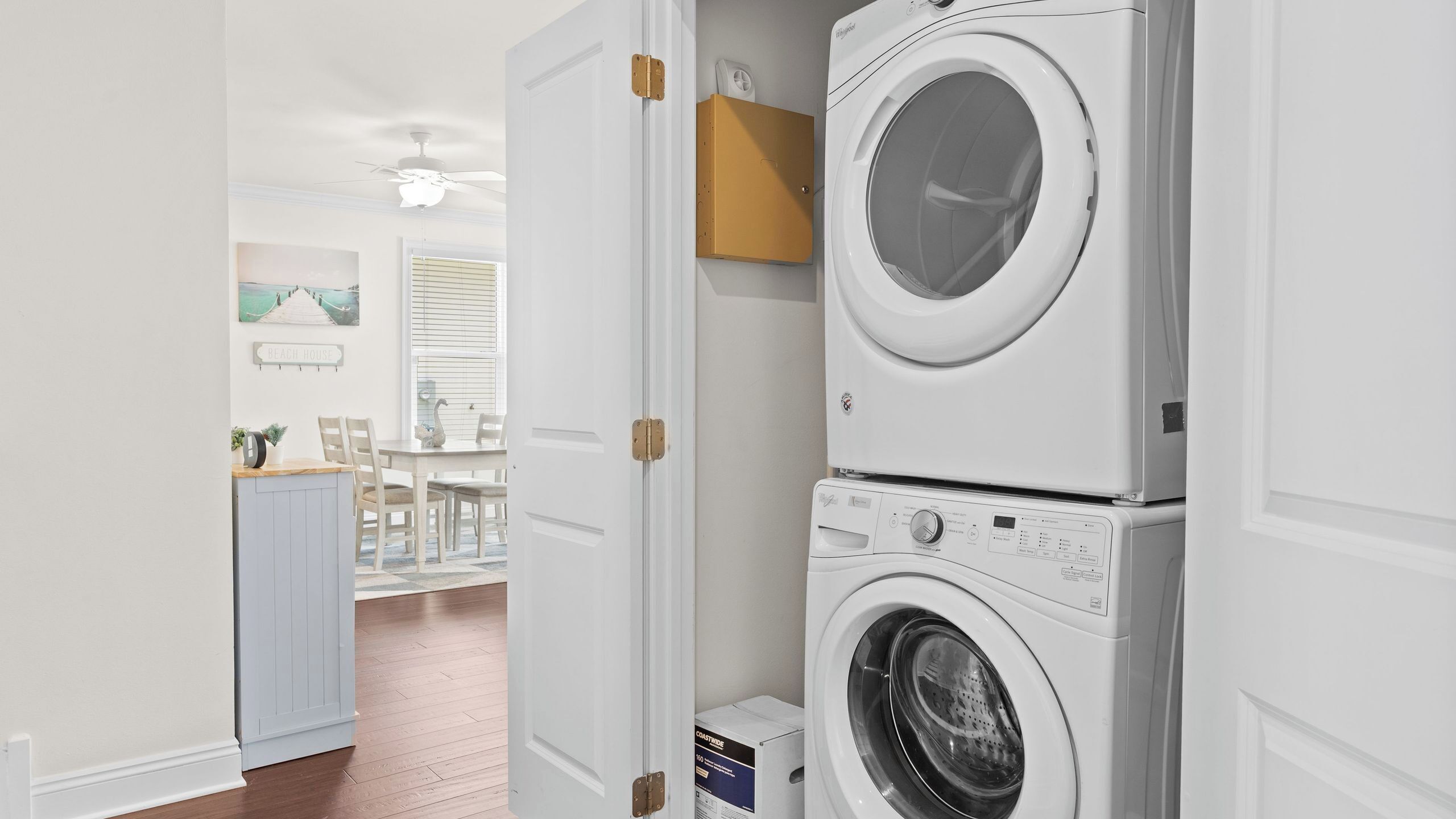 A laundry room with stacked washing machines, a wooden cabinet, and a dining area with a table and chairs.