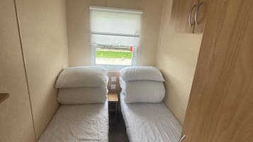 A narrow room with two single beds, a window with a view, and a wooden cabinet.