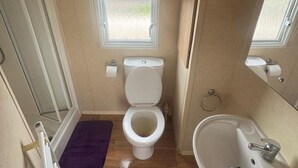 A compact bathroom with a toilet, a sink, and a small window. - 3 Bed Caravan - Sleeps 8 - Pets - Parking (Rhyl)