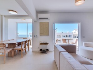 Un salon moderne avec un canapé, une table à manger et des chaises. Une grande fenêtre offre une vue sur la mer.