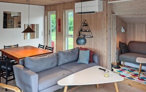 A modern living room with a wooden floor, a grey sofa, a white coffee table, a dining table with chairs, and a large window.
