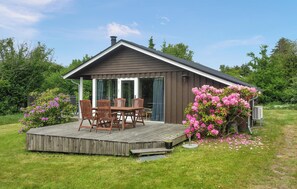 A small wooden cabin with a deck, a dining table, and chairs.