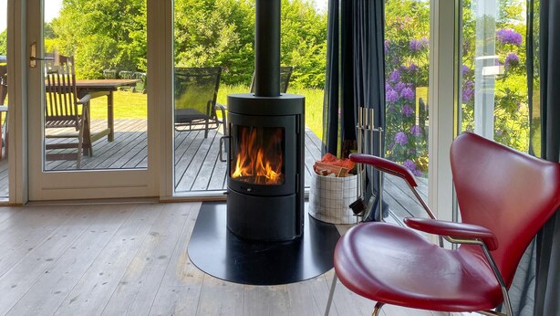 A wood-burning stove in a room with a red chair and a wooden deck visible through a glass door. - Gorgeous home in Glesborg with WiFi (Glesborg)